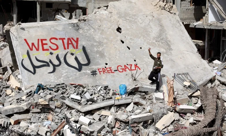 شاب فلسطيني يكتب لافتة "لن نرحل" باللغتين العربية والإنجليزية على جدار مبنى دمرته الهجمات الإسرائيلية