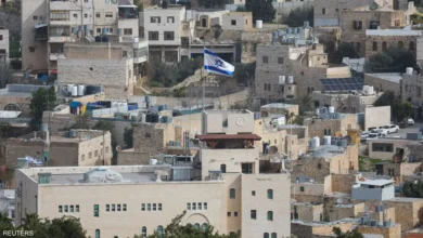 Israeli flag flying above a crowded urban area with closely built houses and rooftops.
