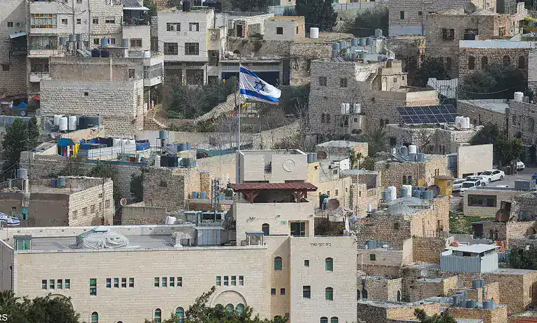 Israeli flag flying above a crowded urban area with closely built houses and rooftops.