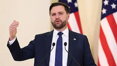 Politician delivering speech at a press event, emphasizing key policies with American flags behind h.