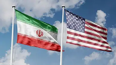 Iran and US flags flying side by side against a blue sky.