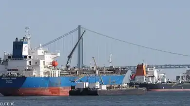 Cargo ships docked at a port with a bridge in the background.